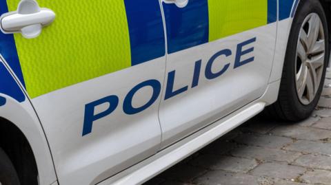 The side of a police car. It is yellow and blue with the word 'police' written on it. 