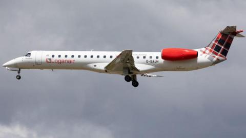 A Loganair plane is seen in mid-flight on a cloudy day. It is a white airplane with a tartan tail.