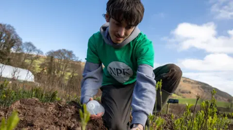 Aelod o dim NPK Recovery yn profi'r pridd yn y feithrinfa goed ger y Fenni
