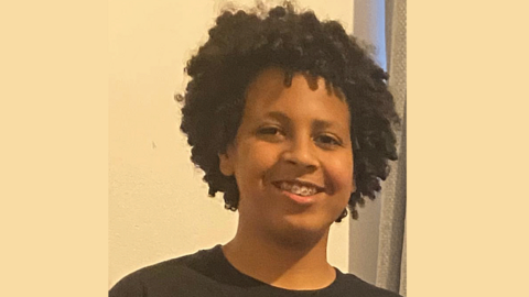 A young man gives a broad smile. He has dark curly hair and wears braces. 