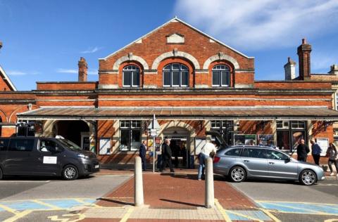 The exterior of Salisbury Train Station with its red brick frontage with passengers and taxis visible