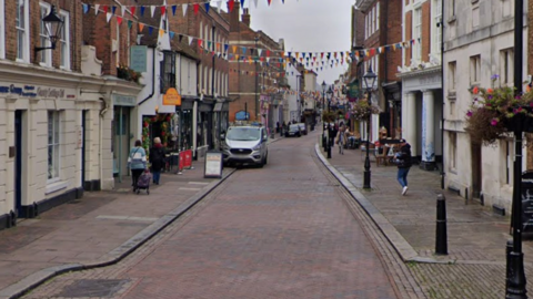 A Google Street image of a high street with shops either side.
