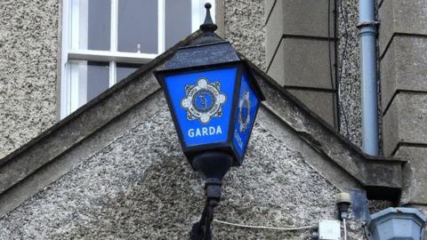 A Garda sign on a blue sign attached to a grey building.