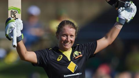 Australia opener Alyssa Healy raises her bat and helmet to celebrate hitting a century in the third women's T20 against Sri Lanka