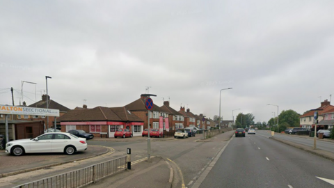Street view image of a long straight road with houses at either side. To the left is the junction which turns onto Windsor Avenue.