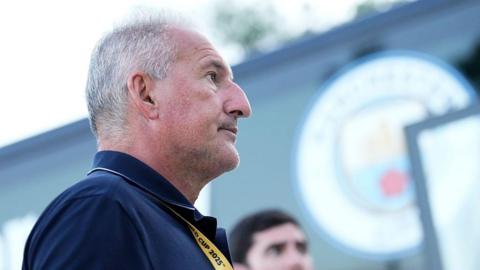 Side profile of Txiki Begiristain looking on before match with Manchester City badge in background