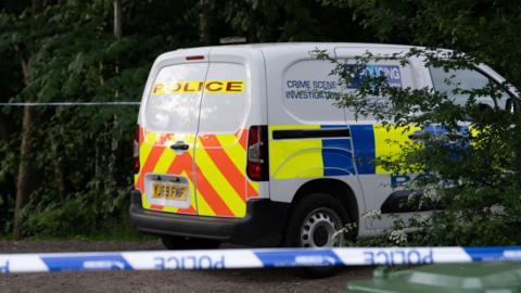 North Yorkshire Police crime scene investigation van behind police tape in wooded area