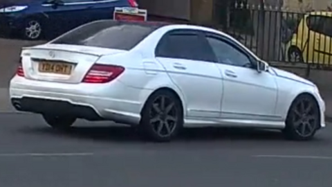 A CCTV still of a white Mercedes being driven along a road.