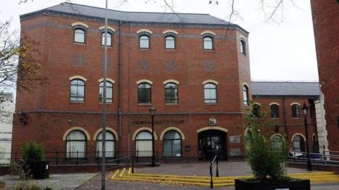 Shot of the entrance to the red-bricked multi-story combined court building in Grimsby. There are yellow markings on the steps leading to the entrance, with potted shrubs in the foreground and to the left hand side of the image.