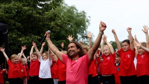 Joe Wicks and pupils with their hands in the air
