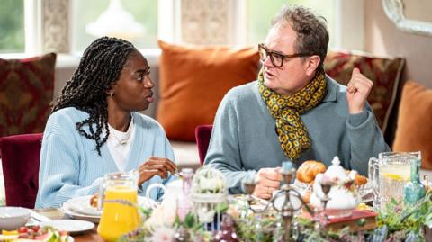 Cat Burns and Alan Carr chat at the breakfast table during the Celebrity Traitors