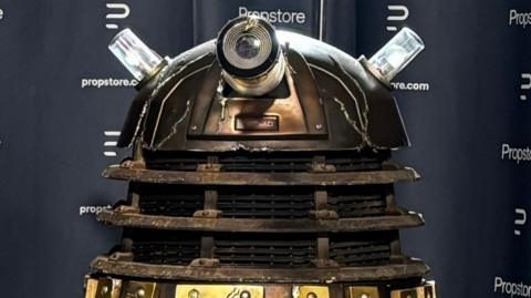 A close up of a battle-damaged Dalek with Propstore branding behind it