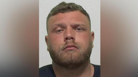 Mugshot of Maddison. He has a muscular head with a short fair beard and short dark hair.