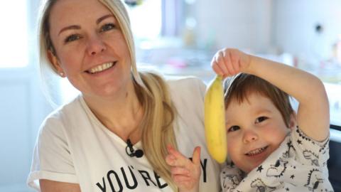 A young child holds a banana while sitting next to his mother.