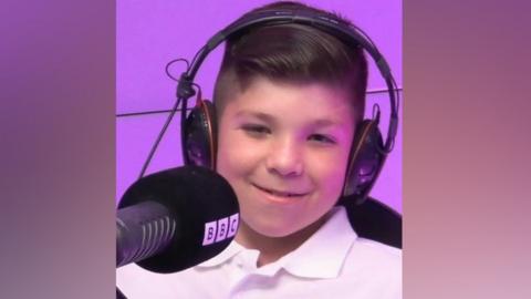 A young boy sits in a Radio studio with headphones on. 