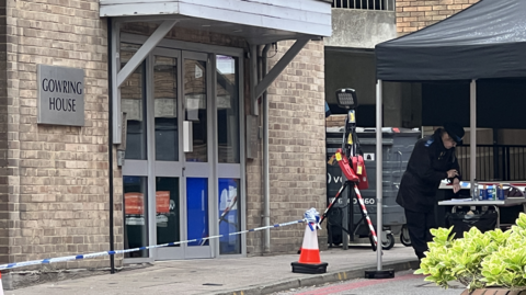 A woman police officer checking her watch outside Gowring House, which is identifiable with a sign that says Gowring House on the left of the picture.