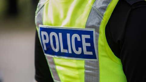 The back of a police officer's uniform, with a green hi-vis jacket saying 'police'