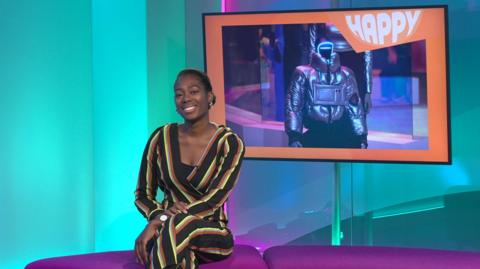 Shanequa in the studio with a robot in the screen