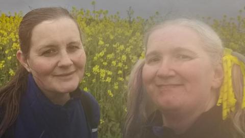 Two woman taking a selfie with yellow flowers behind them