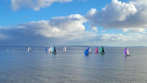 Small sailboats on a grey sea with blue sky and big white clouds above