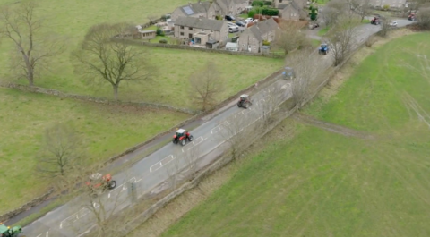 Overhead shot of tractors moving in convoy along a country road