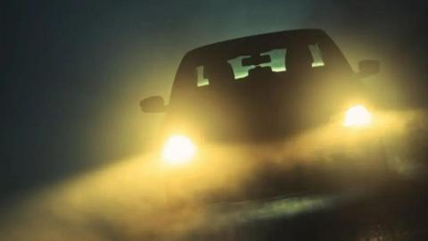 The silhouette of a car in the dark with its headlights on.