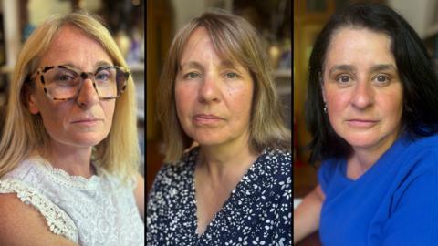 Three women, side by side. The woman on the left has long blond hair, wears tortoise-shell rimmed glasses and a white, sleeveless top. The woman in the middle has brown hair to her shoulders and wears a blue dress with a white floral pattern. The woman on the right has black hair to her shoulders and wears a blue top.