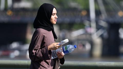 A person walks along a bridge in London carrying a water bottle on Wednesday