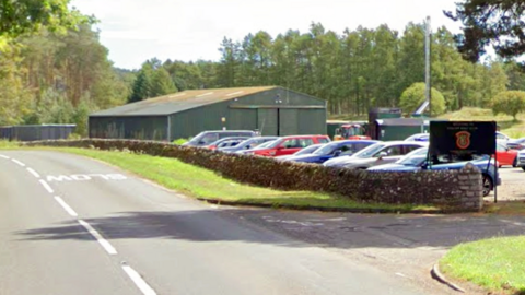 A road with a car park to the right, full of cars, and a sign that says Forfar Golf Club