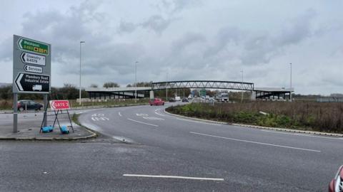 The Mile End roundabout near Oswestry with cars, bushes and road signs in the background.