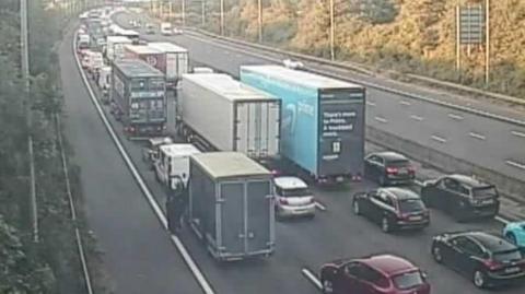 A traffic camera showing a four-lane motorway full of cars at a stand still.
