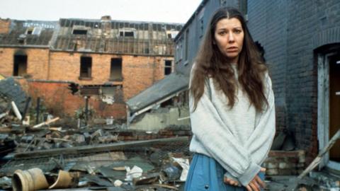 A woman stands in amongst rubble and damaged buildings 