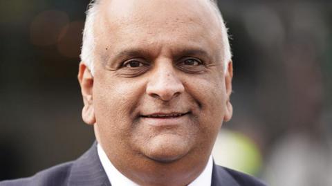 Head and shoulders image of councillor Azhar Ali. He is smiling, has short white hair and is wearing a white shirt and grey striped suit jacket