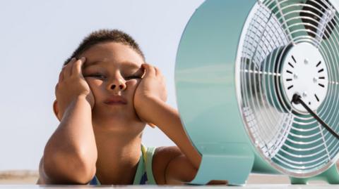 a boy cools himself down in front of a fan