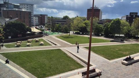grassy square with pathways surrounded by some tall buildings