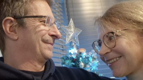 Royal National Lifeboat Institution volunteer Steve Elliott pictured on the left with fiancée Alla Renbenko who agreed to marry him. The pair, who both wear glasses, are looking at each other. A Christmas tree with silver star sits behind the couple.