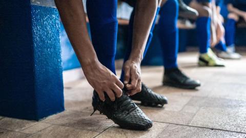 Soccer player tying shoelaces while preparing for match in the locker room