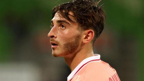 A sweaty brunette man wearing a pink, white and red jersey looks into the distance
