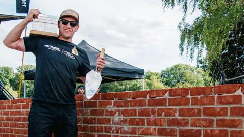 Dale Wherton, with his trophy, stood by the wall he built