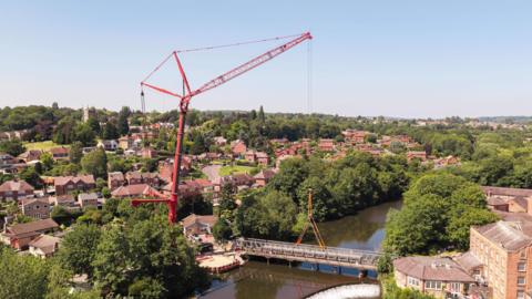 A large red crane lifting a metal bridge from its place