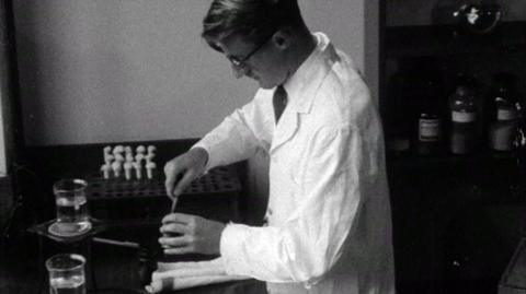 A scientist tests food rations at a table with flasks.