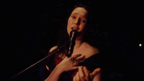 A woman sings a slow song while looking into the camera.