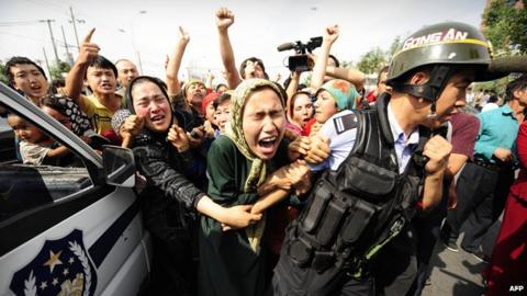 Uighur women grab a riot policemen as they protest in Urumqi in China's far west Xinjiang province on July 7, 2009