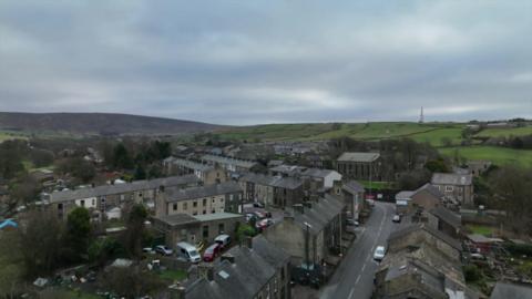 An aerial view of houses and a village road, with rolling green fields in the background 