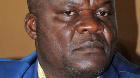 Roger Lumbala looks at the camera with a serious face. He is wearing a blue suit jacket and yellow shirt