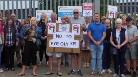 Campaigners standing in front of a metal fence with signs saying 'no to pyrolysis' 