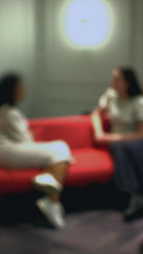Two women sat on a red sofa, with the picture being blurred.