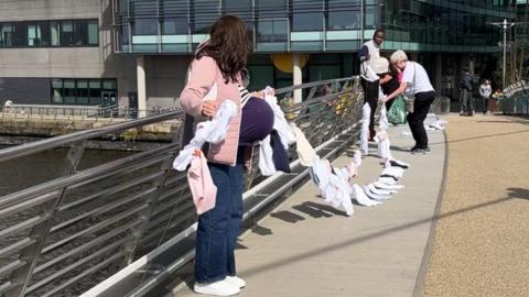 Volunteers from the National Organisation for FASD put up a string of baby vests across a footbridge in Media City. 