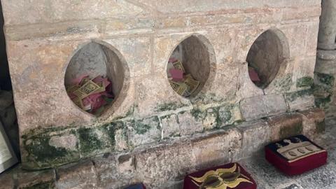 Three large holes are carved in marble beneath a holy shrine, with three kneelers on the floor in front of it.