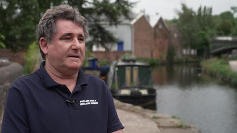 Portland Basin Marina owner Guy Holding. He is standing next to the canal, with a canal boat in the background.